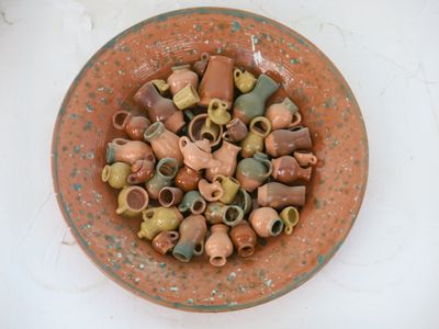 A speckled terracotta bowl filled with dozens of tiny glazed pots, jugs, cups, and teapots